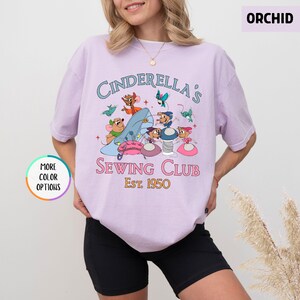 May include: A light purple t-shirt with the text "Cinderella's Sewing Club Est. 1950" and a graphic of Cinderella's mice sewing.