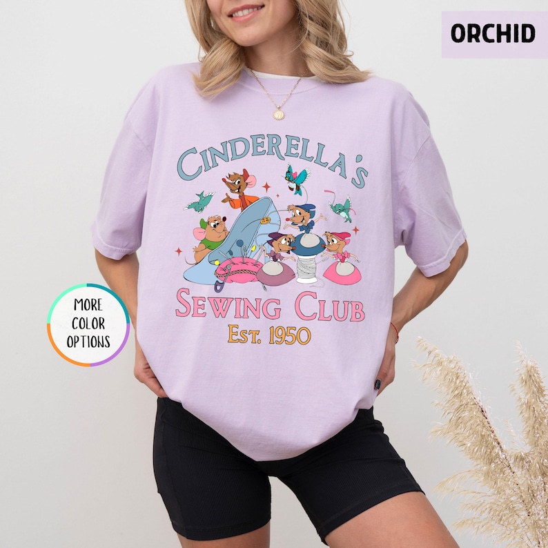 May include: A light purple t-shirt with the text "Cinderella's Sewing Club Est. 1950" and a graphic of Cinderella's mice sewing.