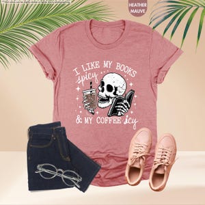 May include: A heather mauve t-shirt with a graphic of a skull holding a book and a cup of coffee. The text on the shirt reads "I like my books spicy & my coffee icy".