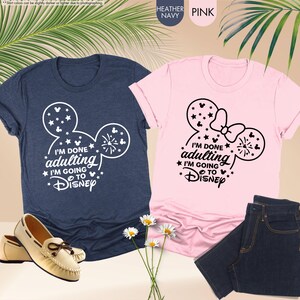 May include: Two t-shirts, one navy blue and one pink, with a white Mickey Mouse silhouette and the text "I'm done adulting I'm going to Disney".