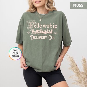 May include: A green t-shirt with a pink graphic of a group of figures walking with the text "Fellowship Est 1954 fast, reliable, precious DELIVERY CO."