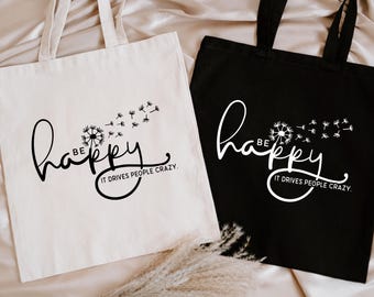 May include: Two tote bags with the text "Be happy. It drives people crazy." printed on them. One bag is white with black text and the other is black with white text.