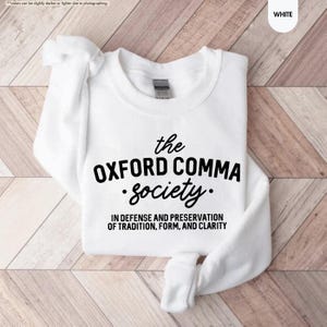 Op de afbeelding: Wit sweatshirt met zwarte tekst die "the OXFORD COMMA society. IN DEFENSE AND PRESERVATION OF TRADITION, FORM, AND CLARITY" luidt.