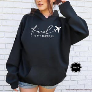 Pu&ograve; includere: Felpa con cappuccio nera con la scritta bianca "travel IS MY THERAPY" e un'immagine di un aereo bianco. La felpa ha una tasca frontale e un cappuccio con coulisse. La parola "BLACK" &egrave; in un distintivo nero a forma di fiore.