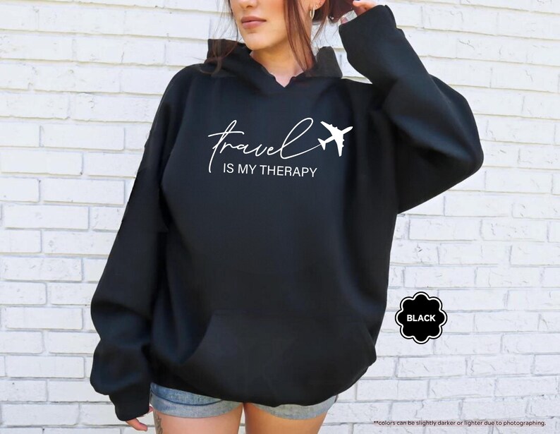 Pu&ograve; includere: Felpa con cappuccio nera con la scritta bianca "travel IS MY THERAPY" e un'immagine di un aereo bianco. La felpa ha una tasca frontale e un cappuccio con coulisse. La parola "BLACK" &egrave; in un distintivo nero a forma di fiore.