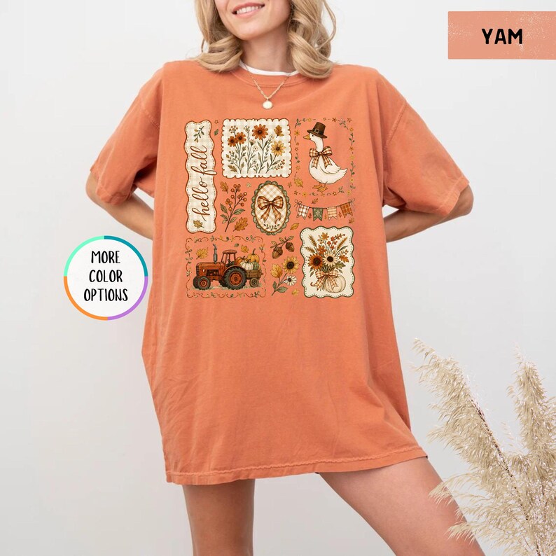 May include: An orange short-sleeved t-shirt featuring a graphic print with the text hello fall. The design includes illustrations of a goose wearing a hat, a tractor, sunflowers, autumn leaves, and a bow, arranged in several rectangular frames.