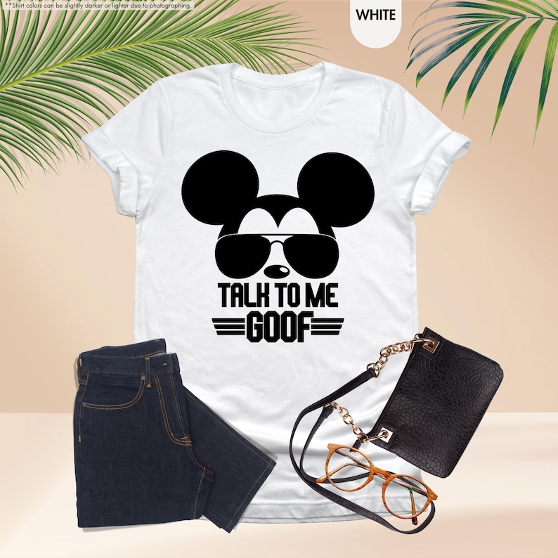 May include: White t-shirt with a black Mickey Mouse graphic wearing sunglasses and the text "TALK TO ME GOOF". The image includes dark blue jeans, a black purse, and a pair of eyeglasses.