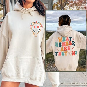 a woman wearing a white hoodie with the words what number are they? on
