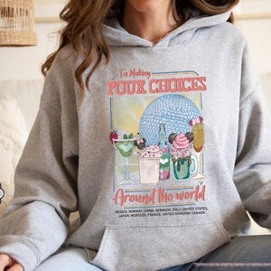 Pu&ograve; includere: Felpa con cappuccio grigio sportivo con grafica colorata. La grafica dice "I'm Making POUR CHOICES Around the World" e presenta illustrazioni di bevande e una sfera blu. Uno stile comodo e casual.