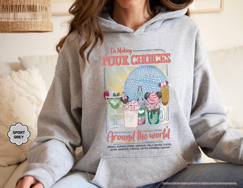Pu&ograve; includere: Felpa con cappuccio grigio sportivo con grafica colorata. La grafica dice "I'm Making POUR CHOICES Around the World" e presenta illustrazioni di bevande e una sfera blu. Uno stile comodo e casual.