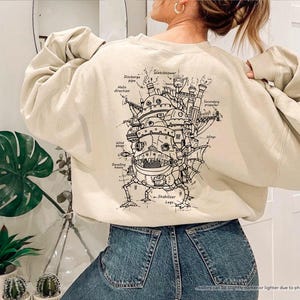 May include: A beige sweatshirt with a black and white illustration of a flying machine on the back. The illustration includes labels for different parts of the machine, such as "Watchtower", "Discharge pipe", and "Stabilizer Legs".