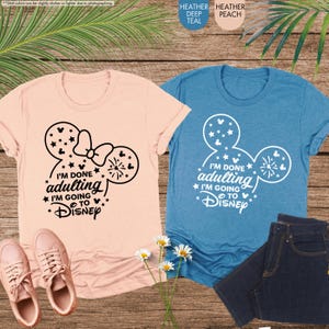 May include: Two t-shirts with a Mickey Mouse ear design. The pink shirt says "I'm done adulting I'm going to Disney" in black text. The blue shirt says "I'm done adulting I'm going to Disney" in white text.