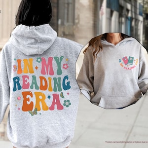 a woman wearing a gray hoodie with the words in my reading era on it