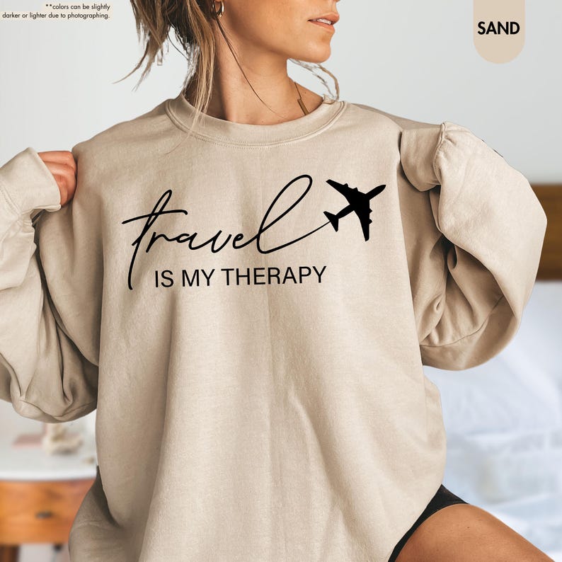 Pu&ograve; includere: Felpa color sabbia con la scritta "travel IS MY THERAPY" in nero e una grafica di un aereo nero. Il top a maniche lunghe &egrave; realizzato in un materiale morbido.