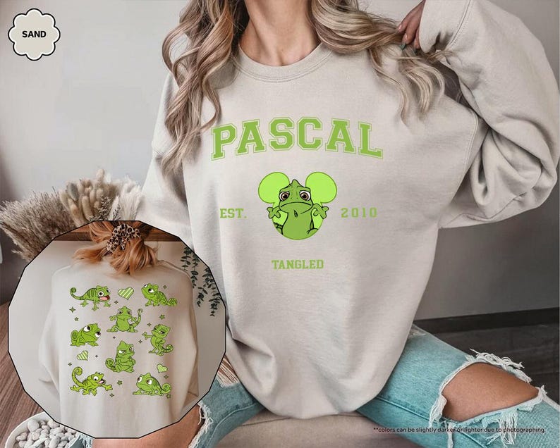 Op de afbeelding: Een zandkleurige sweatshirt met de naam "PASCAL" in groene blokletters, samen met een groen cartoonkameleonontwerp. De sweatshirt bevat ook de tekst "EST. 2010" en "TANGLED". Een kleinere afbeelding van een vergelijkbaar ontwerp is zichtbaar.