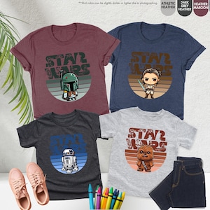 May include: Three t-shirts with different Star Wars characters in a retro style. The shirts are in dark heather, heather grey, and light grey. The characters are Boba Fett, Rey, and Chewbacca.