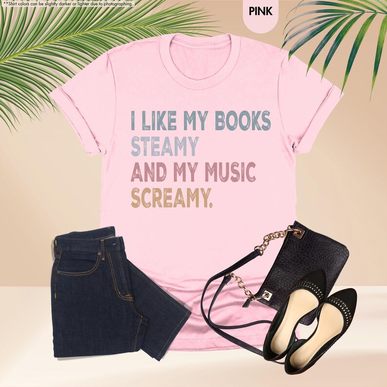 May include: Pink t-shirt with the text "I LIKE MY BOOKS STEAMY AND MY MUSIC SCREAMY." The image also includes a pair of dark wash jeans, a black purse with a gold chain strap, and black flats.