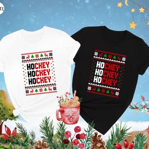 May include: Two Christmas themed t-shirts, one white and one black, with the text "HOCKEY" repeated three times in red on each shirt. The shirts have a red and green snowflake pattern.