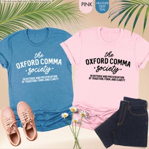 Op de afbeelding: Twee T-shirts met de tekst "the OXFORD COMMA Society. IN DEFENSE AND PRESERVATION OF TRADITION, FORM, AND CLARITY" erop gedrukt. E&eacute;n shirt is roze en de andere is blauw.