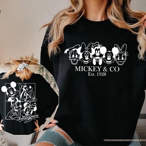 May include: Black sweatshirt featuring a white graphic of Mickey Mouse and friends, with the text "MICKEY & CO Est. 1928". The back of the sweatshirt also has a white graphic of Mickey Mouse and friends.