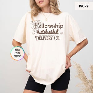 May include: A cream colored t-shirt with a brown graphic of the Fellowship of the Ring walking with the text "Fellowship" above and "EST 1954 fast, reliable, precious DELIVERY CO." below.