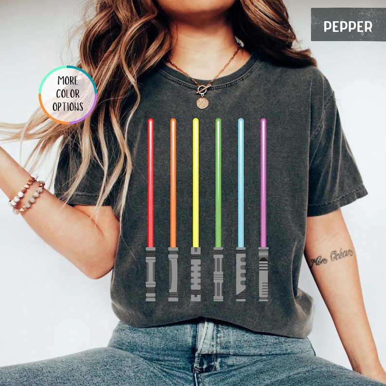 K&ouml;nnte beinhalten: Dunkelgraues T-Shirt mit einem Regenbogen-Lichtschwert-Design. Die Lichtschwerter sind rot, orange, gelb, gr&uuml;n, blau und lila. Auf dem T-Shirt steht das Wort "Pepper".