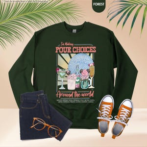 Pu&ograve; includere: Una felpa verde foresta con la scritta "I'm Making Pour Choices Around the World". La grafica presenta vari cocktail e dessert. L'immagine include anche un paio di jeans blu, scarpe da ginnastica arancioni e occhiali.
