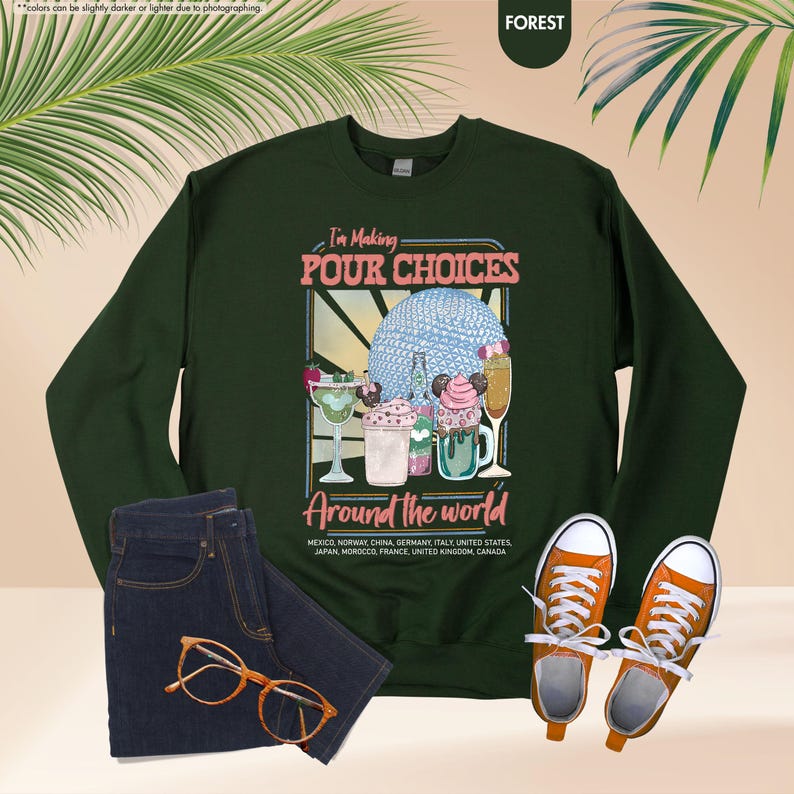 Pu&ograve; includere: Una felpa verde foresta con la scritta "I'm Making Pour Choices Around the World". La grafica presenta vari cocktail e dessert. L'immagine include anche un paio di jeans blu, scarpe da ginnastica arancioni e occhiali.