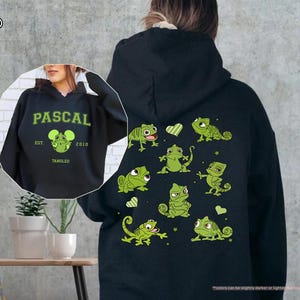 Op de afbeelding: Zwarte hoodie met een groen Pascal-ontwerp uit de film Rapunzel. De voorkant heeft het woord "PASCAL" en een Pascal-afbeelding. De achterkant toont meerdere groene Pascal-illustraties en harten.