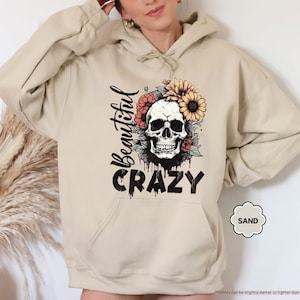 May include: A beige hoodie with a skull graphic and floral accents. The text "Beautiful Crazy" is printed on the hoodie.