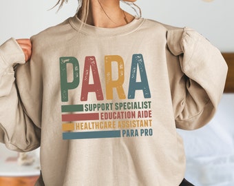 May include: A beige sweatshirt with the word "PARA" in large, colorful letters. Below the word are the words "Support Specialist", "Education Aide", "Healthcare Assistant", and "Para Pro" in smaller, colorful letters.