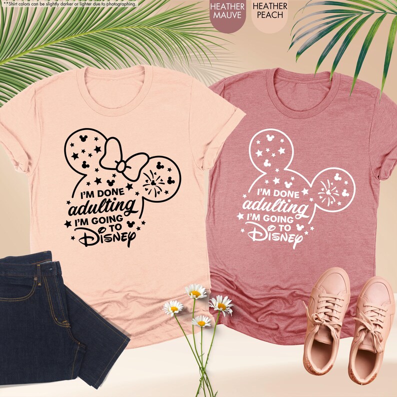 May include: Two t-shirts with a Mickey Mouse ear design and the text "I'm done adulting I'm going to Disney". The shirt on the left is a light pink heather color and the shirt on the right is a darker pink heather color.