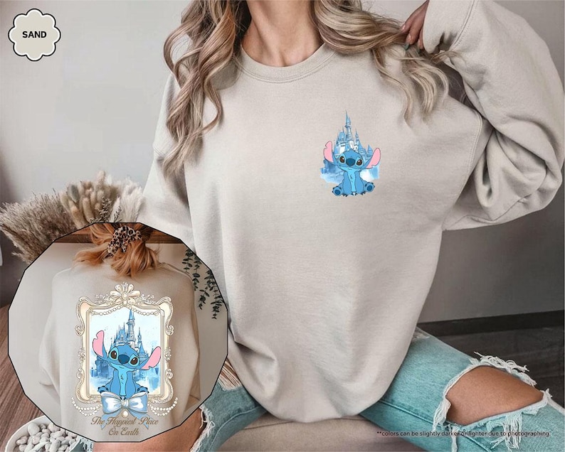May include: Sand-colored sweatshirt featuring a blue cartoon character with a castle design. The sweatshirt has a crew neck and long sleeves. The design includes the text "The Happiest Place on Earth" in a decorative frame.