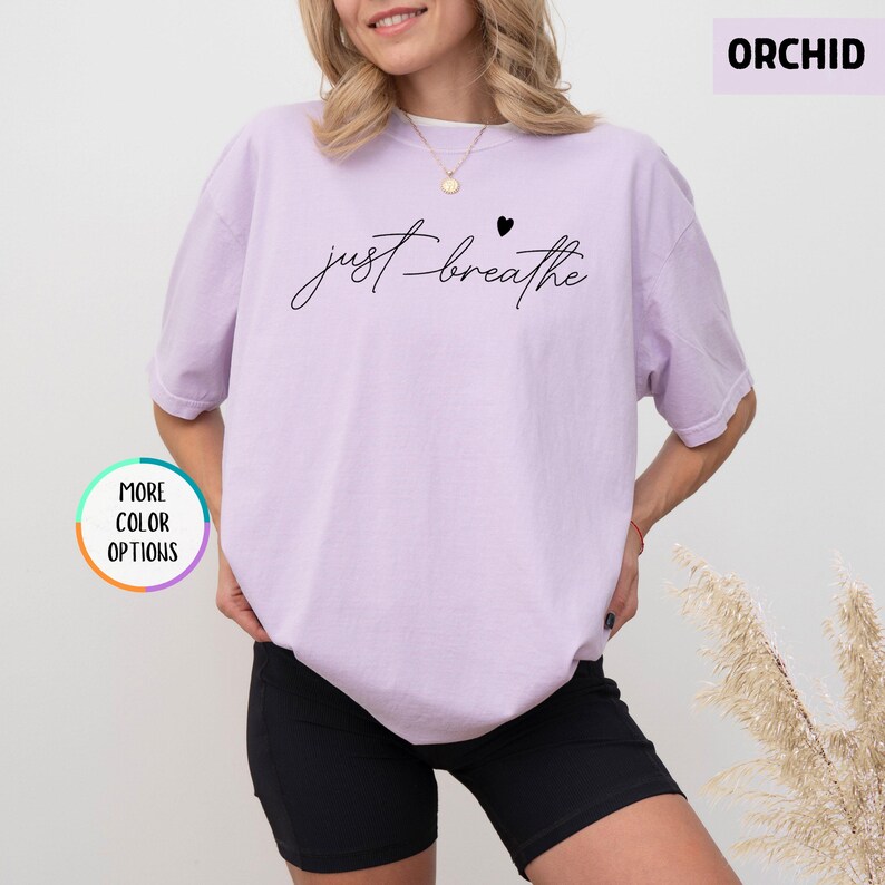 May include: A lavender t-shirt with the text "just breathe" in black script with a small black heart above the word "breathe".