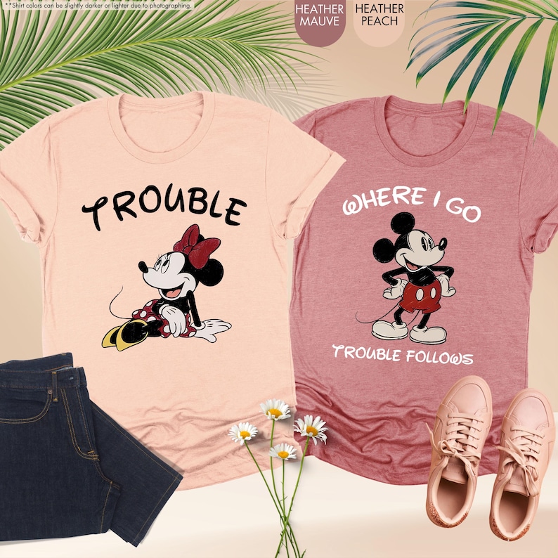 May include: Two heather t-shirts, one peach and one mauve, featuring cartoon characters. The peach shirt has "TROUBLE" and a Minnie Mouse graphic. The mauve shirt says "WHERE I GO TROUBLE FOLLOWS" with a Mickey Mouse graphic. Also shown are jeans and shoes.