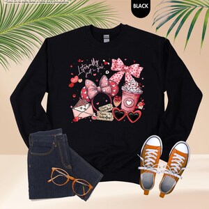 May include: Black sweatshirt with a graphic design including a pink bow, heart-shaped sunglasses, and the text "Literally just a girl." The design also features hearts, a coffee cup, and "Xoxo Valentine."