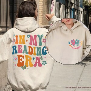 a person wearing a white hoodie with the words in my reading era on it