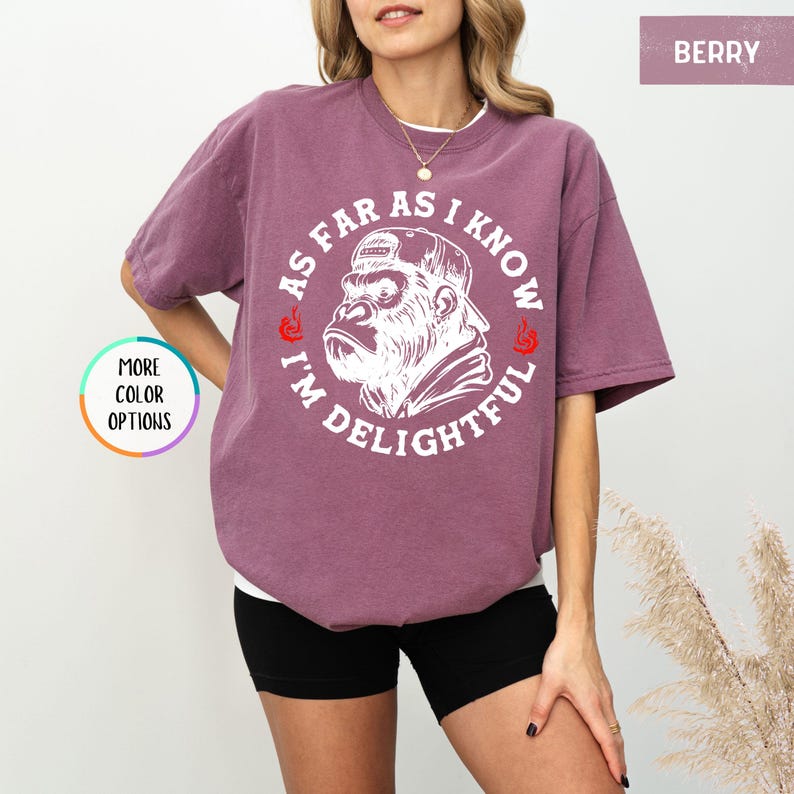 May include: Berry-colored t-shirt with a white graphic of a gorilla wearing a cap, surrounded by the text "AS FAR AS I KNOW I'M DELIGHTFUL". The shirt has short sleeves and a relaxed fit.