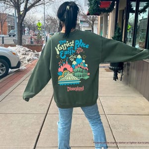 Pu&ograve; includere: Felpa verde con una grafica colorata del castello di Disneyland e il testo "The Happiest Place on Earth" e "Disneyland" in bianco.