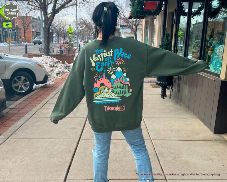 Pu&ograve; includere: Felpa verde con una grafica colorata del castello di Disneyland e il testo "The Happiest Place on Earth" e "Disneyland" in bianco.