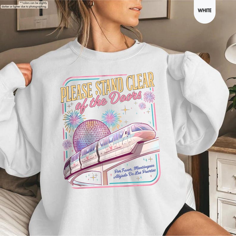 May include: White sweatshirt with a colorful graphic featuring a monorail, a geodesic sphere, and the text "PLEASE STAND CLEAR of the Doors." The design includes fireworks and the Spanish phrase "Por Favor, Mant&eacute;ngase Alejado De Las Puertas."