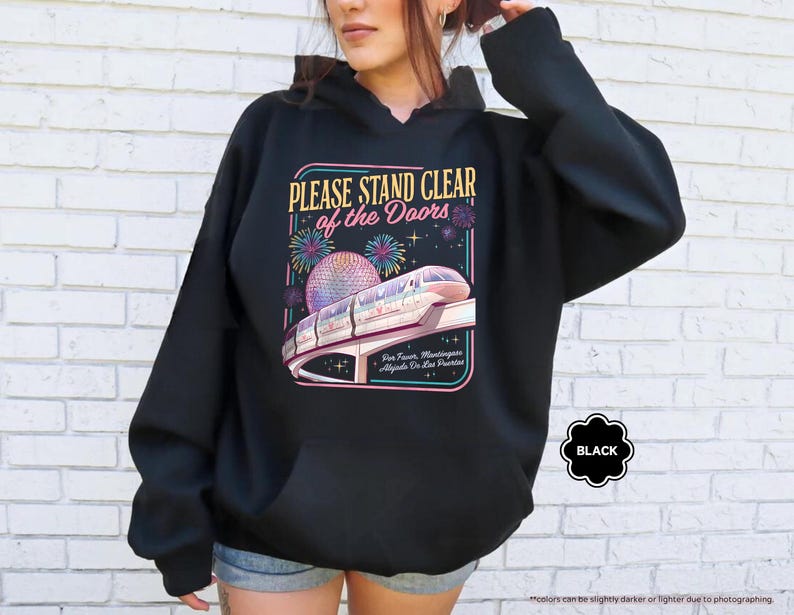 May include: Black hooded sweatshirt with a graphic featuring a monorail, fireworks, and the text "PLEASE STAND CLEAR of the Doors." The design includes a colorful illustration of a futuristic train and a large sphere. The word "BLACK" is also visible.