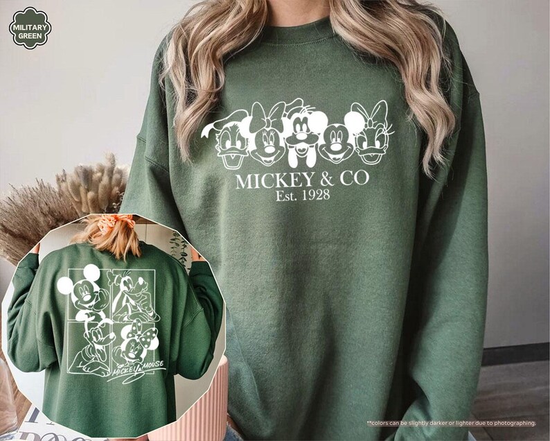 May include: Military green sweatshirt featuring a white graphic of Mickey Mouse and friends. The front design includes the text "MICKEY & CO Est. 1928". The back of the sweatshirt also has a white graphic of Mickey Mouse and friends.