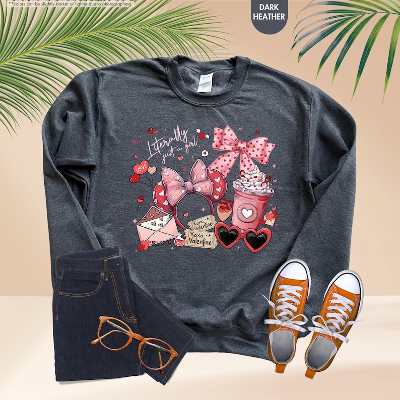 May include: Dark grey sweatshirt featuring the text "Literally just a girl" with a pink bow, heart-shaped sunglasses, a coffee cup, and a Minnie Mouse ear headband. The image also shows jeans and orange trainers.