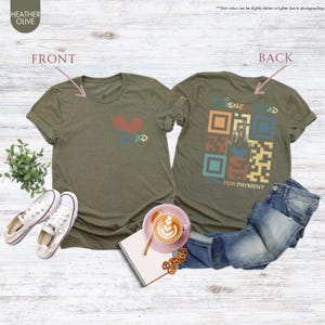 May include: A green t-shirt with a heart and the word "DAD" on the front. The back of the shirt has a retro-style QR code with the words "DISNEY" and "SCAN FOR PAYMENT".