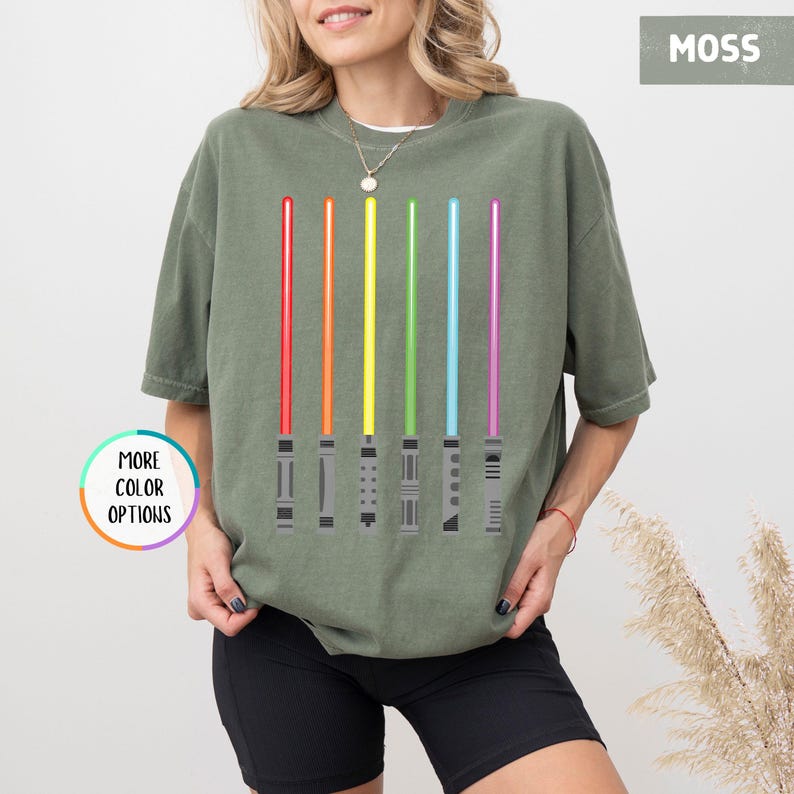 K&ouml;nnte beinhalten: Moosgr&uuml;nes T-Shirt mit Regenbogen-Lichtschwertern. Die Lichtschwerter sind rot, orange, gelb, gr&uuml;n, blau und lila. Das Shirt hat den Text "MORE COLOR OPTIONS" in einem Kreis.