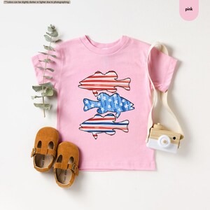 a pink shirt with fish on it next to a pair of shoes