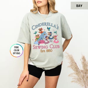 May include: A light green t-shirt with a graphic of mice sewing a blue slipper. The text "Cinderella's Sewing Club Est. 1950" is printed on the shirt.