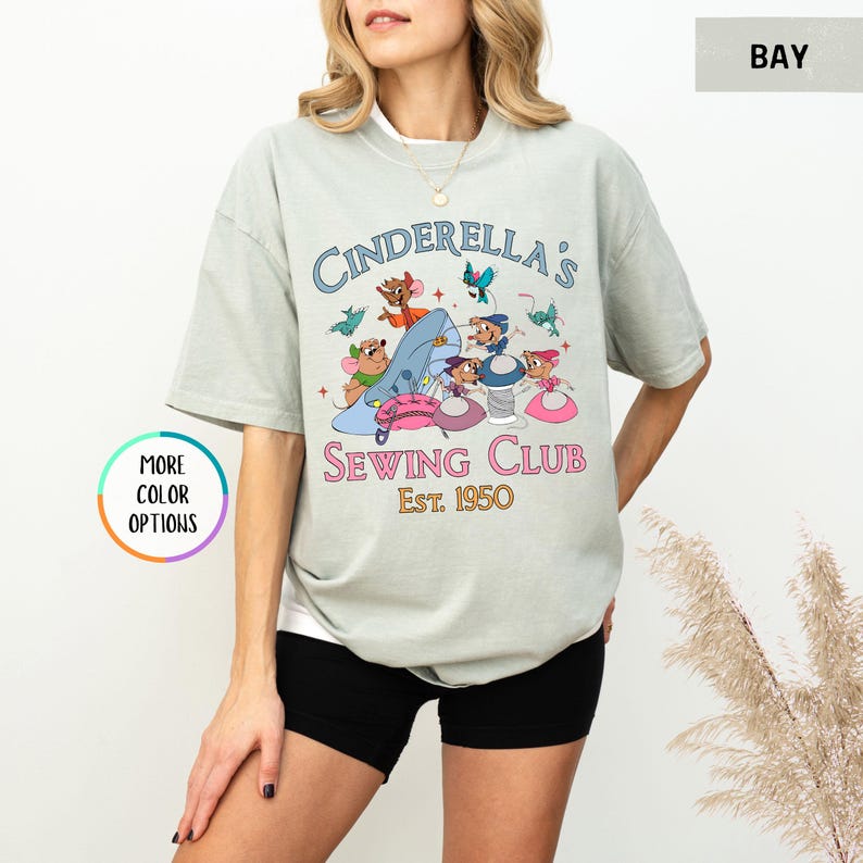 May include: A light green t-shirt with a graphic of mice sewing a blue slipper. The text "Cinderella's Sewing Club Est. 1950" is printed on the shirt.