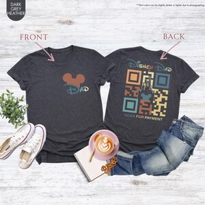 May include: Dark heather grey t-shirt with a Mickey Mouse head and the word "DAD" on the front. The back of the shirt has a retro-style QR code with the words "Disney Dad" and "Scan for Payment".